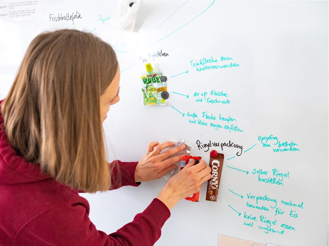 Lisa Carlotta Weimar untersucht gemeinsam mit Schüler*innen den Inhalt der Brotdose, um Abfallvermeidungspotenziale zu ermitteln (Foto: Torsten Stapel)