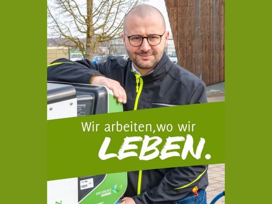 Christian Mehnert lehnt an einer Wallbox für E-Autos. Im Vordergrund des Bildes steht auf grünem Hintergrund: "Wir arbeiten, wo wir LEBEN." (Foto: Torsten Stapel)